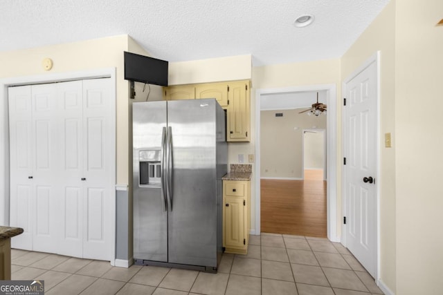 kitchen with a textured ceiling, stainless steel refrigerator with ice dispenser, cream cabinetry, and light tile patterned floors
