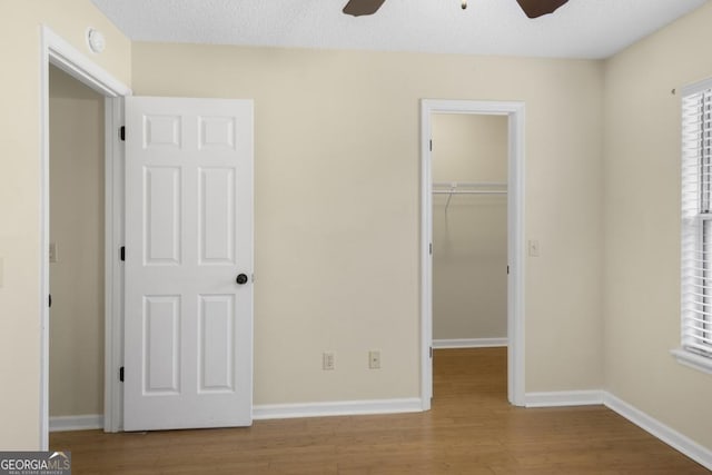 unfurnished bedroom featuring a walk in closet, wood finished floors, a closet, and baseboards
