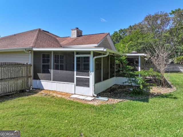 rear view of house featuring a chimney, a sunroom, fence, and a yard