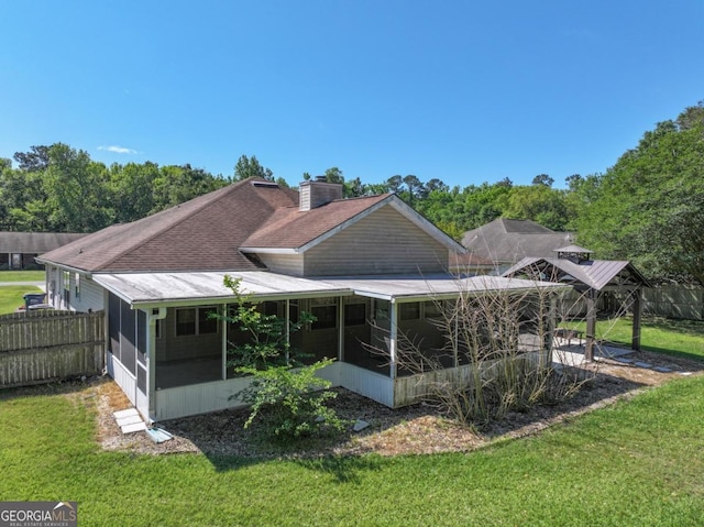rear view of property with fence, a chimney, a sunroom, and a yard