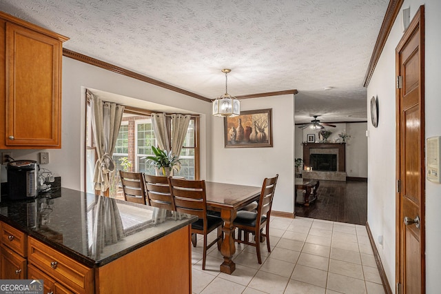 dining room with crown molding, baseboards, a fireplace with raised hearth, light tile patterned flooring, and ceiling fan