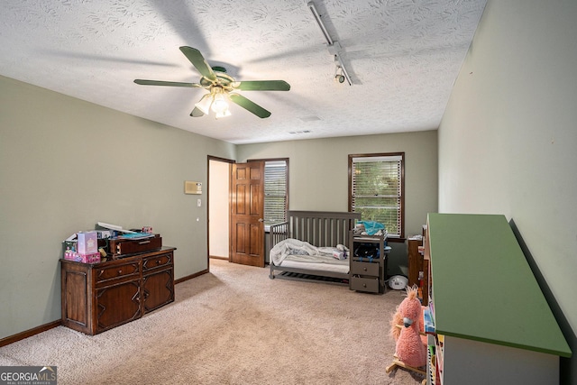 bedroom with a textured ceiling, light colored carpet, a ceiling fan, rail lighting, and baseboards