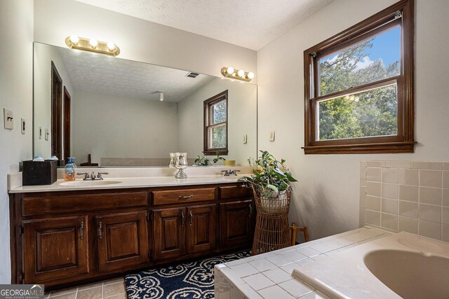 full bath featuring a textured ceiling, a bathtub, and double vanity