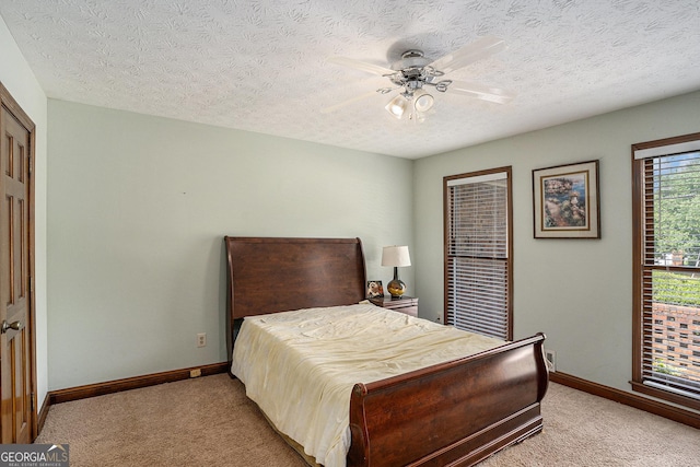 bedroom featuring light carpet, baseboards, a textured ceiling, and ceiling fan