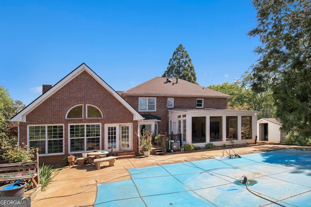 rear view of property featuring brick siding, a sunroom, a patio area, a chimney, and a covered pool