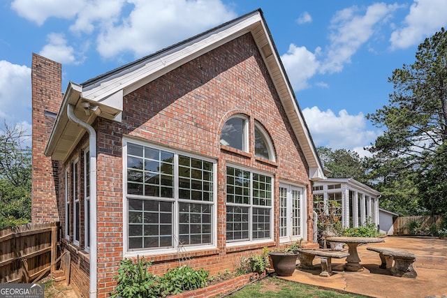 view of side of property featuring brick siding, fence, and a chimney