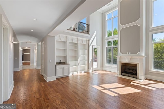 6509 Lily Trl, Fairburn, GA 30213 - unfurnished living room featuring wood finished floors, a fireplace with flush hearth, built in shelves, and a high ceiling
