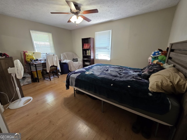 bedroom featuring ceiling fan, multiple windows, a textured ceiling, and light wood-style floors