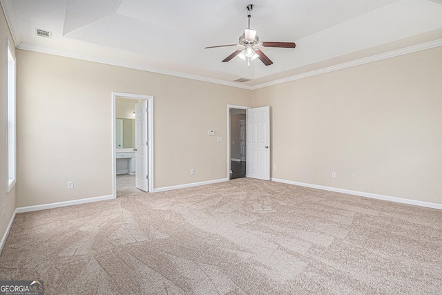 unfurnished bedroom with a tray ceiling, light colored carpet, baseboards, ornamental molding, and visible vents