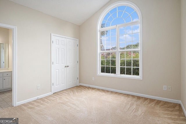 unfurnished bedroom featuring carpet floors, a closet, vaulted ceiling, and baseboards