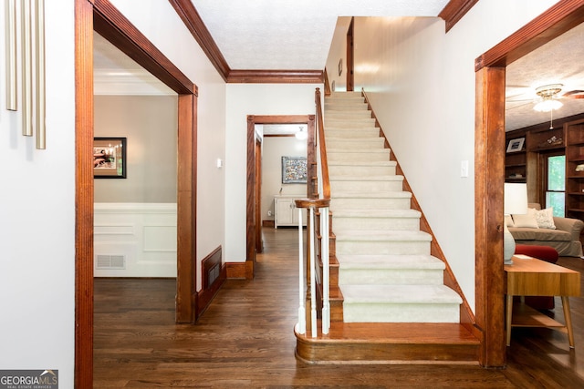 staircase with ornamental molding, wood finished floors, visible vents, and a textured ceiling