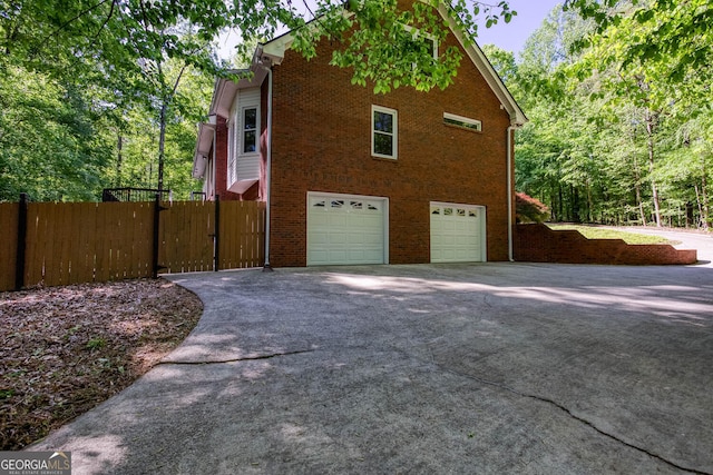 view of property exterior with brick siding, an attached garage, driveway, and fence