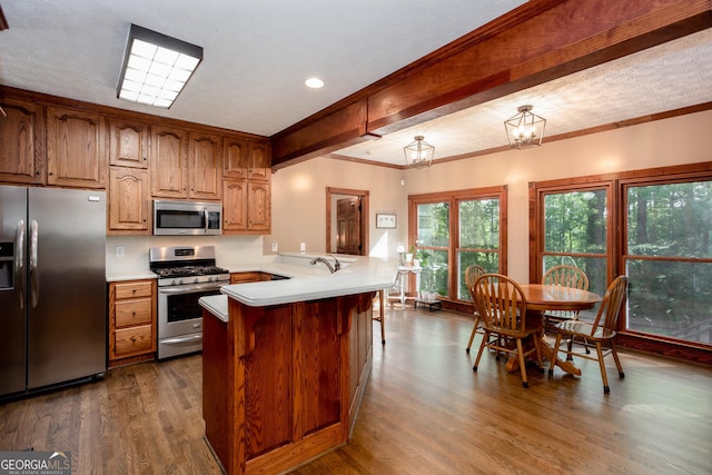 kitchen featuring brown cabinets, light countertops, a peninsula, appliances with stainless steel finishes, and dark wood-type flooring