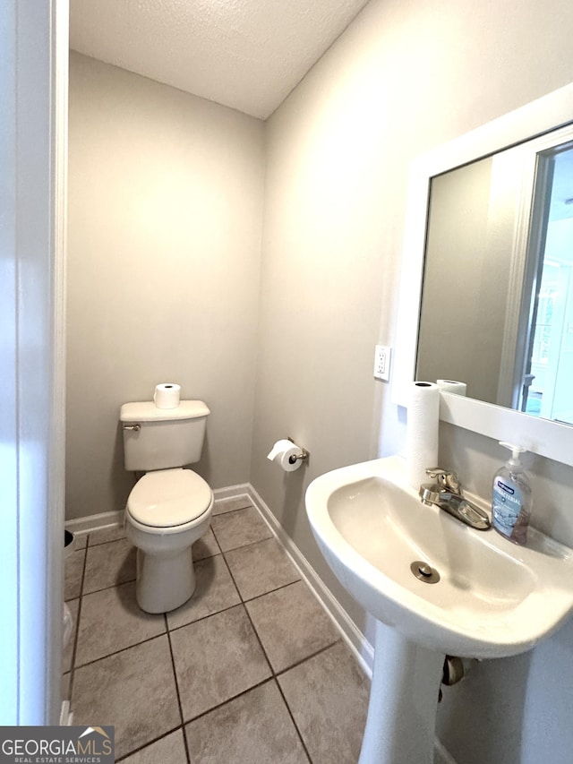 bathroom featuring baseboards, a textured ceiling, tile patterned floors, and toilet