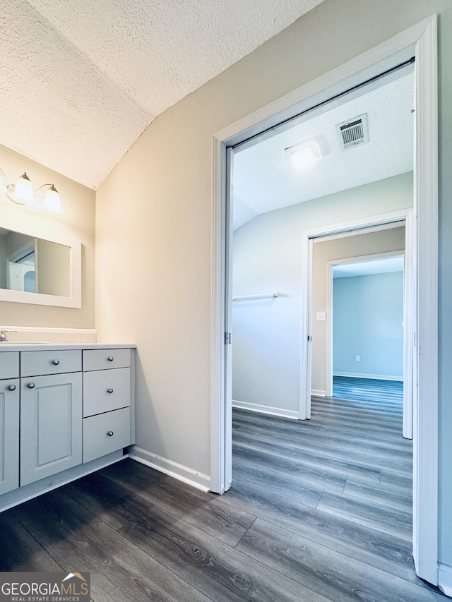 bathroom with vanity, a textured ceiling, wood finished floors, lofted ceiling, and visible vents