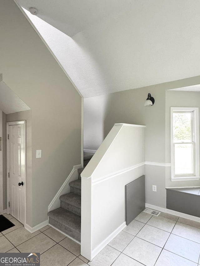 stairs with tile patterned flooring, baseboards, vaulted ceiling, and visible vents
