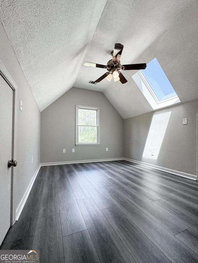 bonus room featuring vaulted ceiling with skylight, a ceiling fan, a textured ceiling, dark wood finished floors, and baseboards