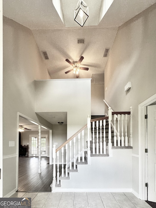 stairway with visible vents, ceiling fan, tile patterned flooring, and high vaulted ceiling
