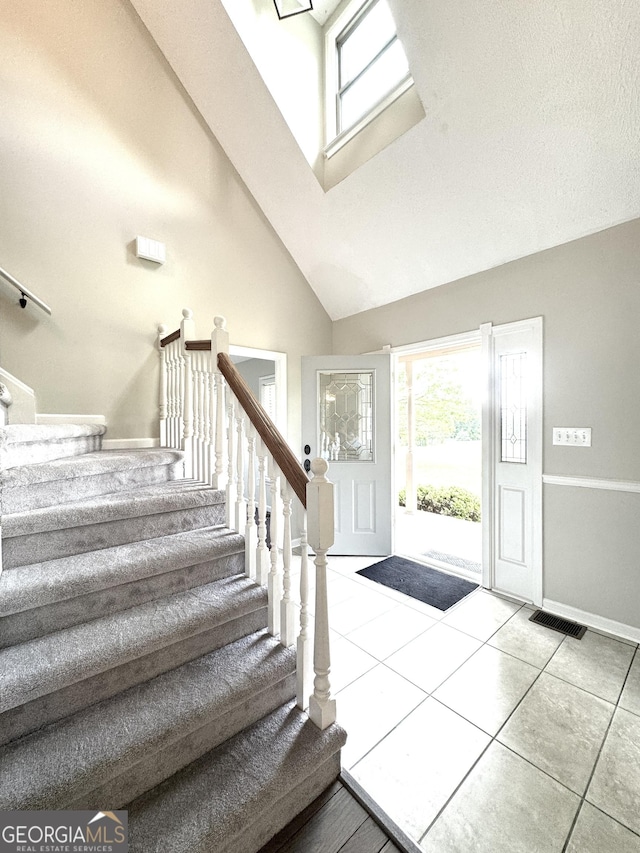 foyer entrance featuring visible vents, high vaulted ceiling, tile patterned floors, and stairway