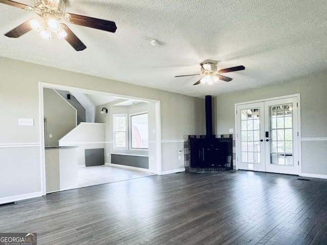 unfurnished living room featuring french doors, a ceiling fan, a textured ceiling, a wood stove, and wood finished floors