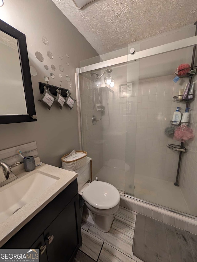 bathroom with vanity, toilet, a textured ceiling, and a stall shower