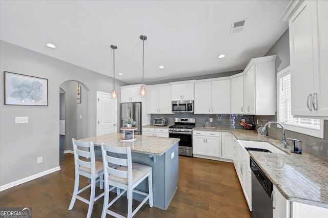 kitchen featuring stainless steel appliances, visible vents, a sink, arched walkways, and decorative backsplash