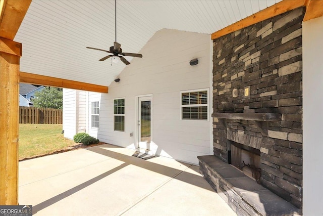 view of patio with fence, an outdoor stone fireplace, and a ceiling fan