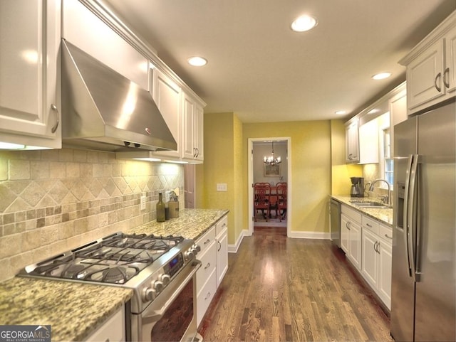 kitchen featuring baseboards, wall chimney exhaust hood, white cabinetry, a sink, and appliances with stainless steel finishes