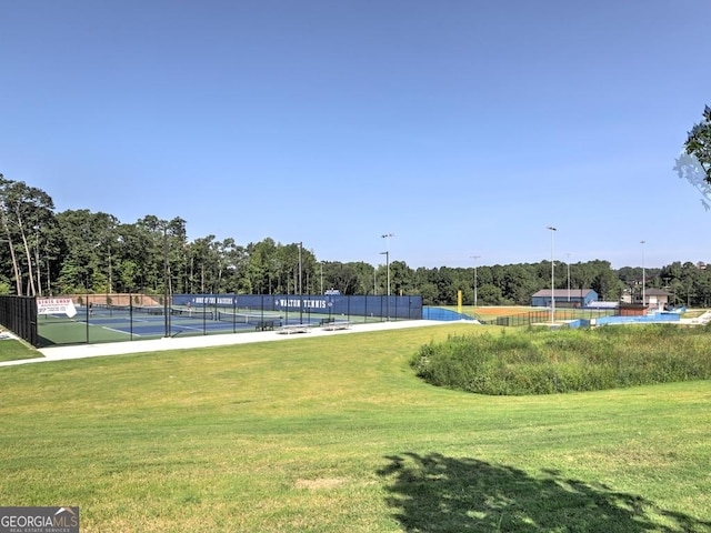 view of property's community featuring a lawn, a tennis court, and fence