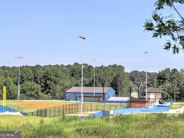 view of tennis court with a yard, a view of trees, and fence