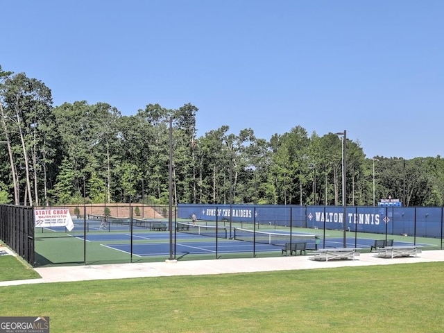 view of tennis court with a lawn and fence