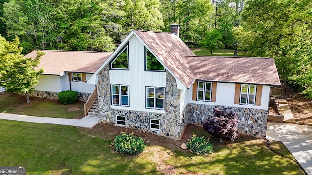 exterior space featuring stone siding, a chimney, a yard, and stairway