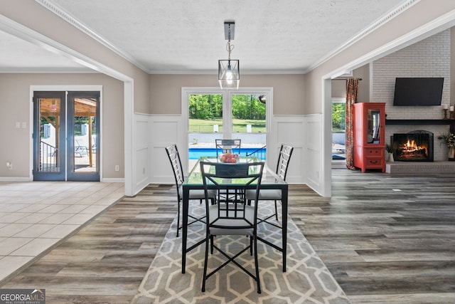 dining space with wood finished floors, french doors, wainscoting, a fireplace, and a textured ceiling