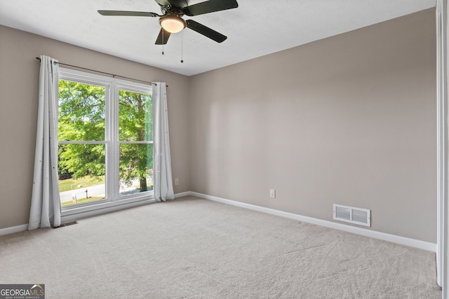 carpeted spare room with visible vents, baseboards, and ceiling fan