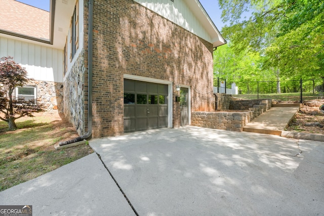 view of property exterior with driveway, stone siding, and fence