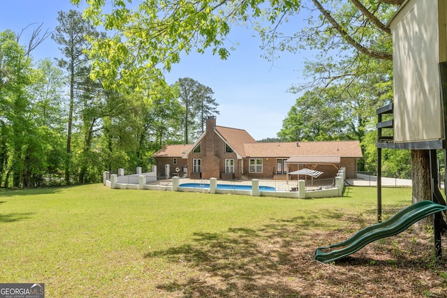 rear view of house featuring a chimney, an outdoor pool, a yard, and a playground