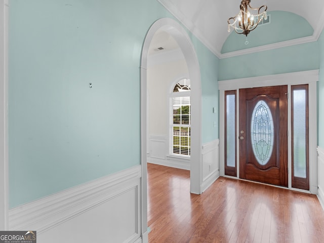 foyer entrance featuring wainscoting, a chandelier, wood-type flooring, arched walkways, and vaulted ceiling