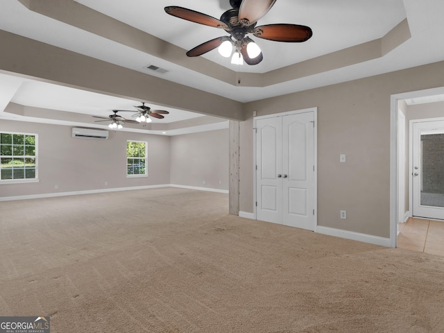 empty room with a raised ceiling, an AC wall unit, ceiling fan, and baseboards