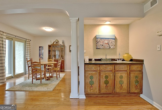 dining area featuring light wood-style floors, wet bar, baseboards, visible vents, and ornate columns