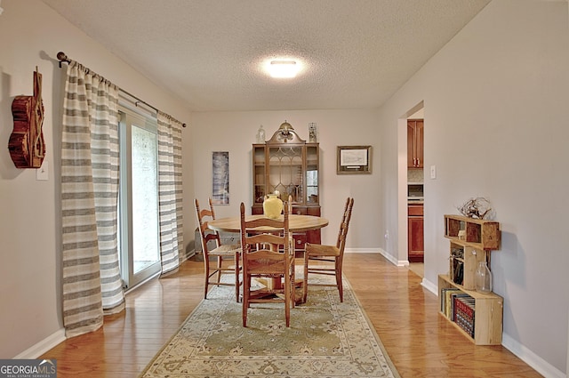 dining area with light wood-type flooring, baseboards, and a textured ceiling