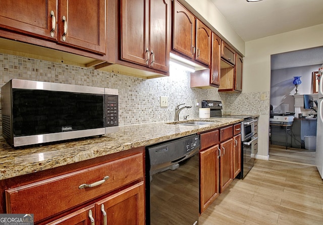 kitchen with a sink, decorative backsplash, brown cabinets, light stone counters, and appliances with stainless steel finishes