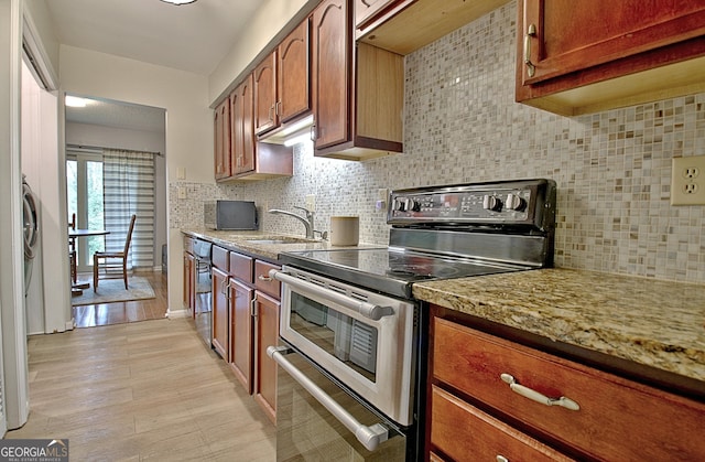 kitchen featuring a sink, light wood-style floors, decorative backsplash, range with two ovens, and brown cabinetry