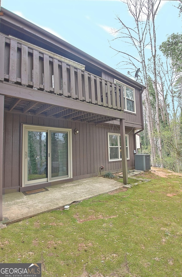 rear view of property featuring board and batten siding, a lawn, central AC, and a patio
