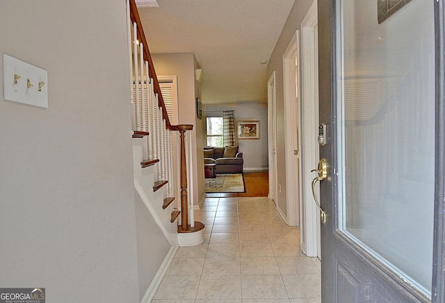 hallway featuring baseboards, light tile patterned flooring, and stairs