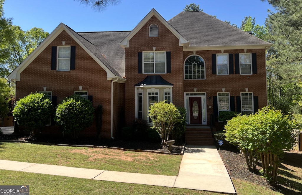 colonial-style house with roof with shingles, a front lawn, and brick siding
