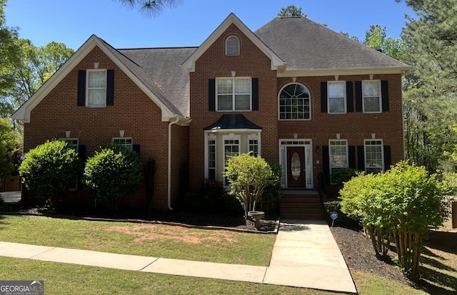 colonial-style house with roof with shingles, a front lawn, and brick siding