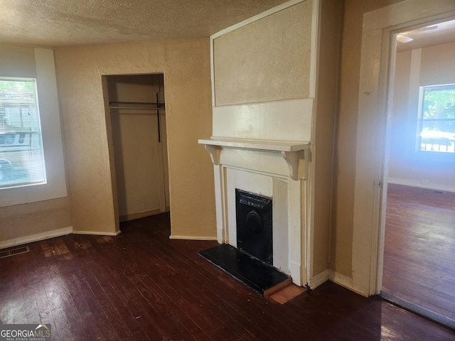4 Maple St, Porterdale, GA 30014 - unfurnished living room featuring dark wood-style floors, visible vents, baseboards, a fireplace with raised hearth, and a textured wall
