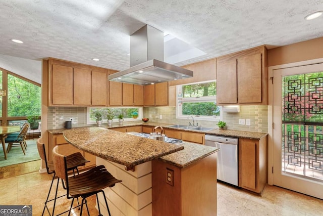 kitchen with a sink, a textured ceiling, island exhaust hood, stainless steel appliances, and backsplash