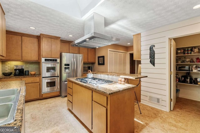 kitchen with a center island, a textured ceiling, island range hood, appliances with stainless steel finishes, and visible vents