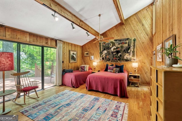 bedroom featuring wood finished floors, lofted ceiling with beams, wooden walls, rail lighting, and access to exterior